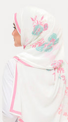 A woman shown from the side wearing a white hijab with pink border trim and teal floral print, against a plain light background.