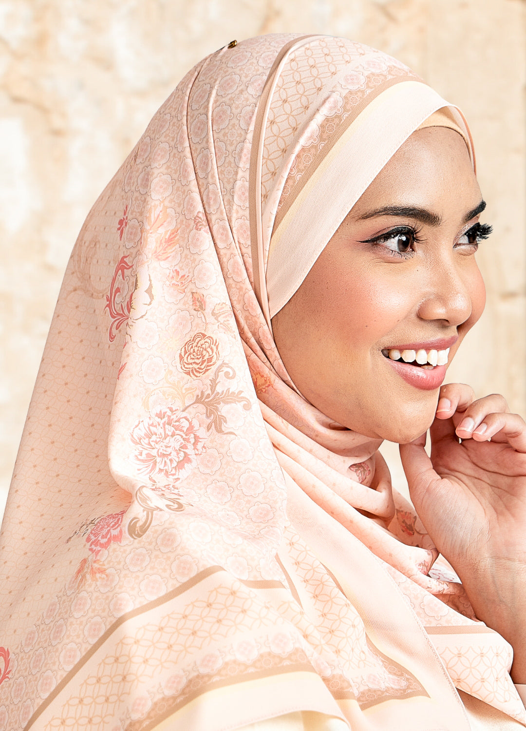 Woman wearing a light pink hijab with floral patterns against a beige background