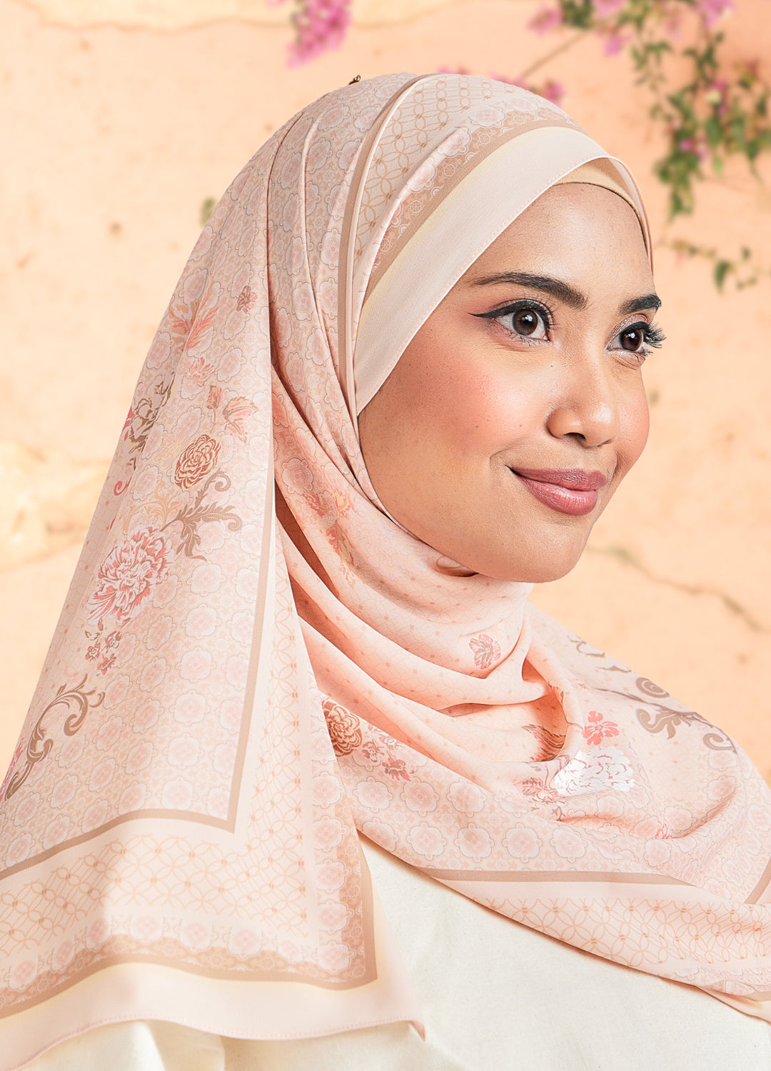 Woman wearing a pink hijab with floral patterns against a soft, blurred background