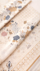 A folded piece of cream-colored fabric with a traditional floral print in muted blue, gold, and pink, featuring a matching gold geometric border.