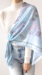 A light blue scarf with a delicate floral pattern in pink, purple, and green, styled over a white ribbed turtleneck sweater and light-wash jeans.