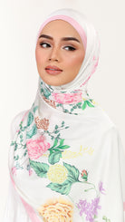 A woman wearing a white hijab with a pastel pink undercap and a colorful floral print featuring pink, yellow, and green roses and leaves, set against a plain white background.