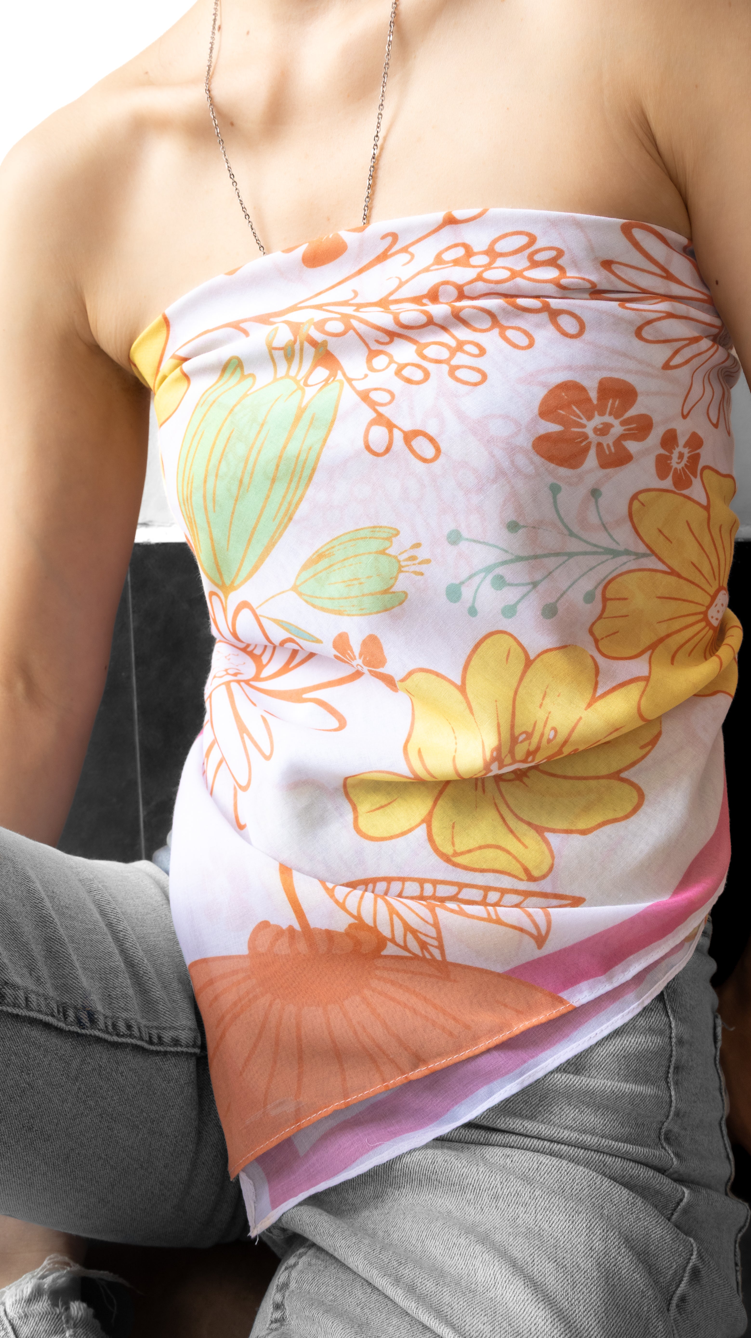 A close-up of a person wearing a white strapless tube top with a colorful retro floral print in orange, yellow, and light green, paired with gray jeans.