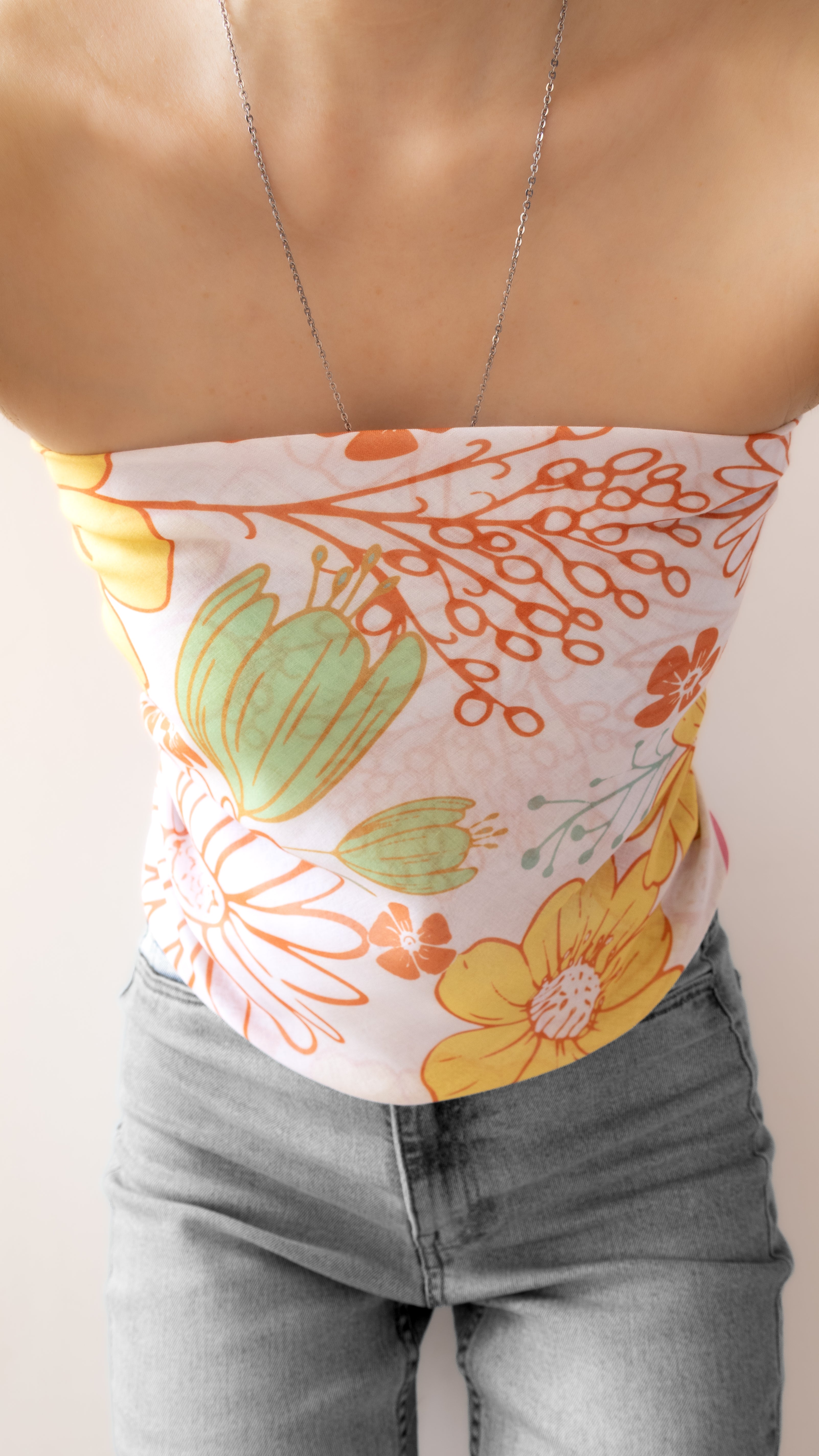 A close-up of a person wearing a strapless tube top with a retro floral print in orange, yellow, and green on a white background, paired with gray jeans.