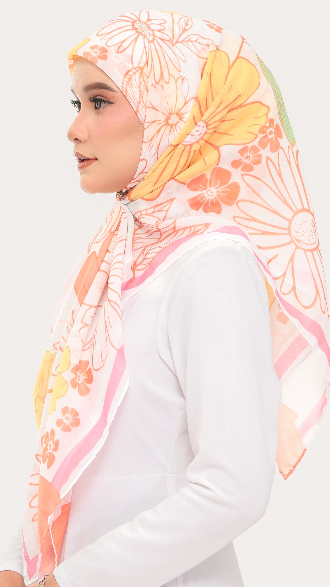 A woman in profile wearing a white long-sleeve top and a sheer floral hijab with large daisy-like flowers in orange, pink, and yellow on a white background.