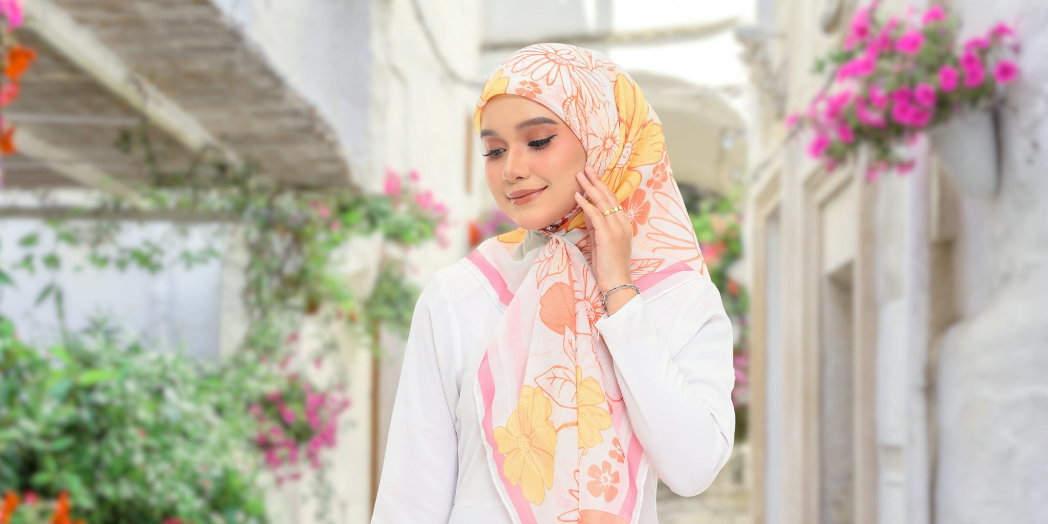 Woman wearing a floral headscarf and white outfit in a garden setting