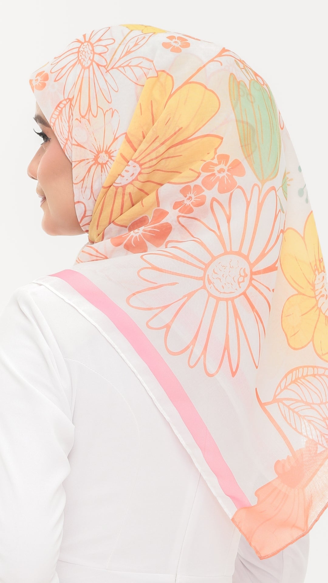 A woman shown from the side wearing a sheer white hijab with a colorful floral print in yellow, orange, and peach, featuring a pink border.