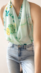 A mint green halter-style scarf with a yellow and green floral print, worn by a model paired with light-wash blue jeans.
