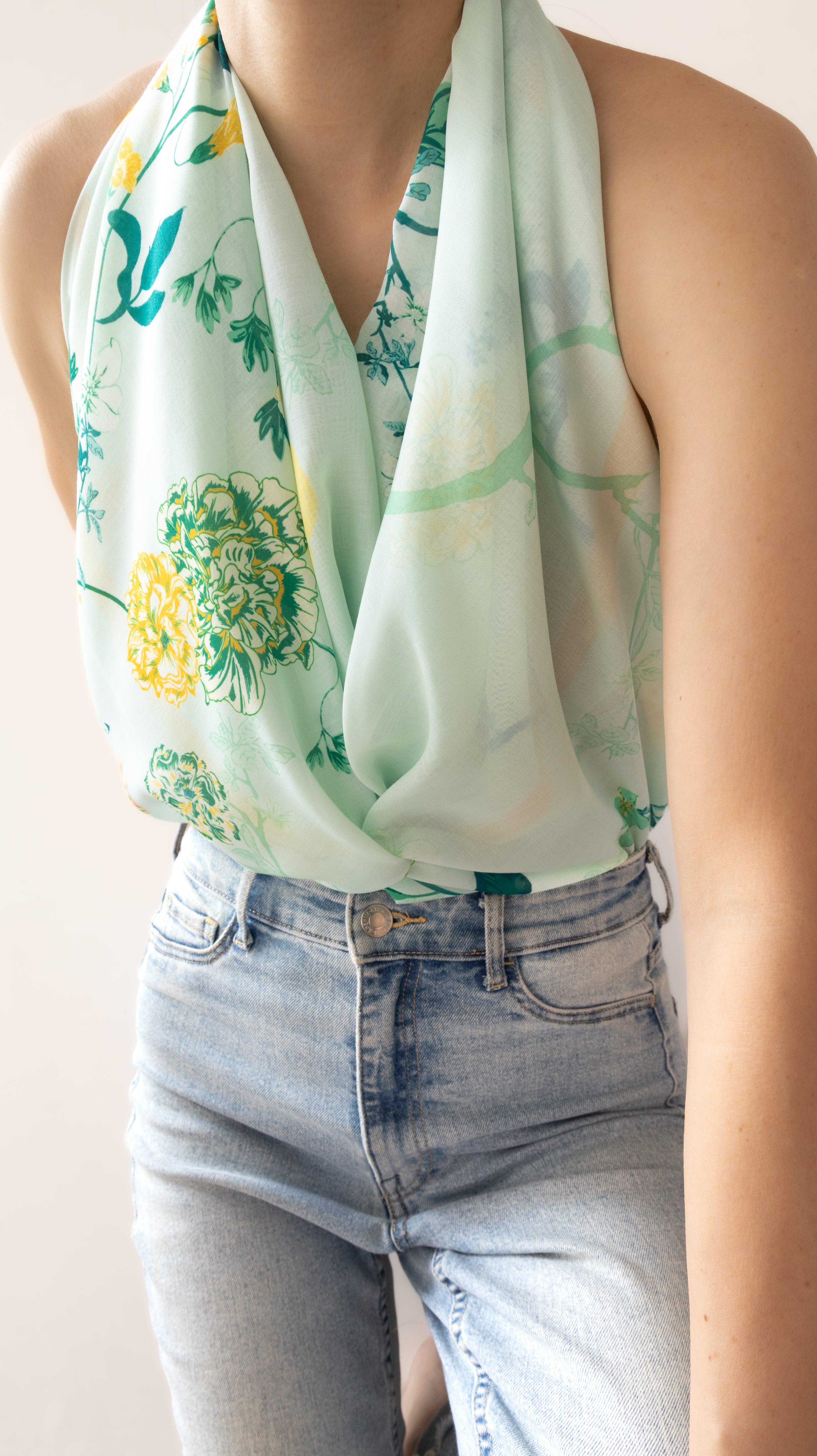 A mint green halter-style scarf with a yellow and green floral print, worn by a model paired with light-wash blue jeans.